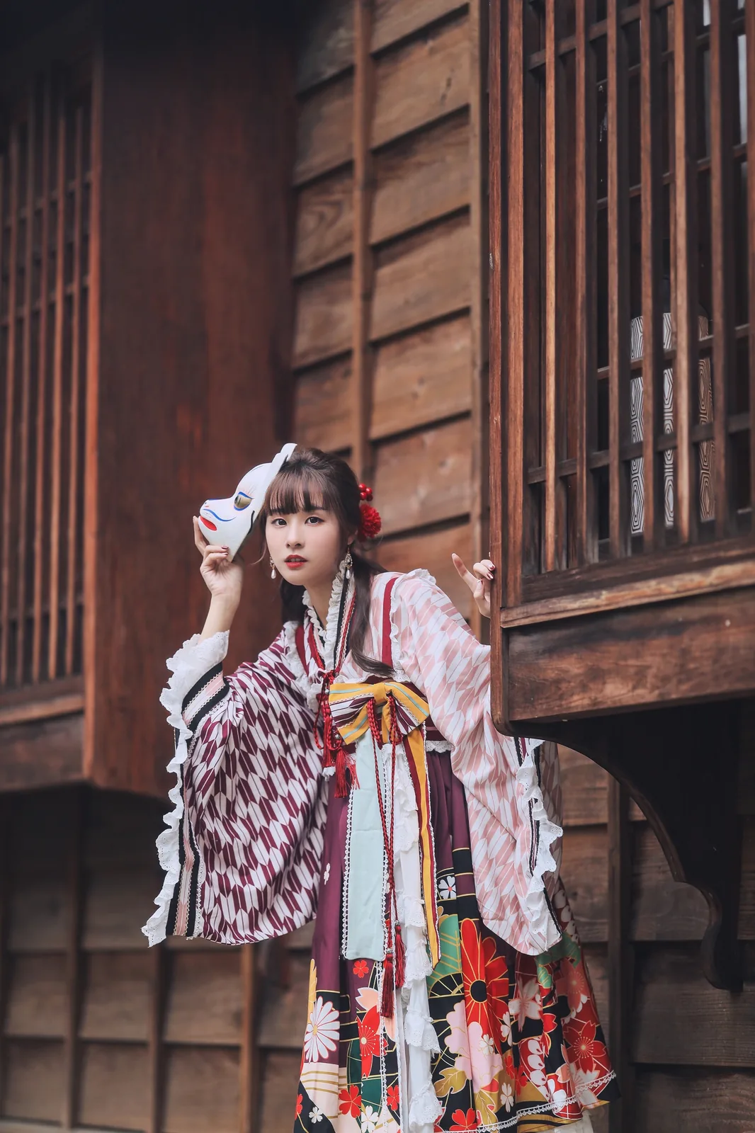泥泥汝穿粉色与深红几何纹和风服装在木窗旁手持狐面